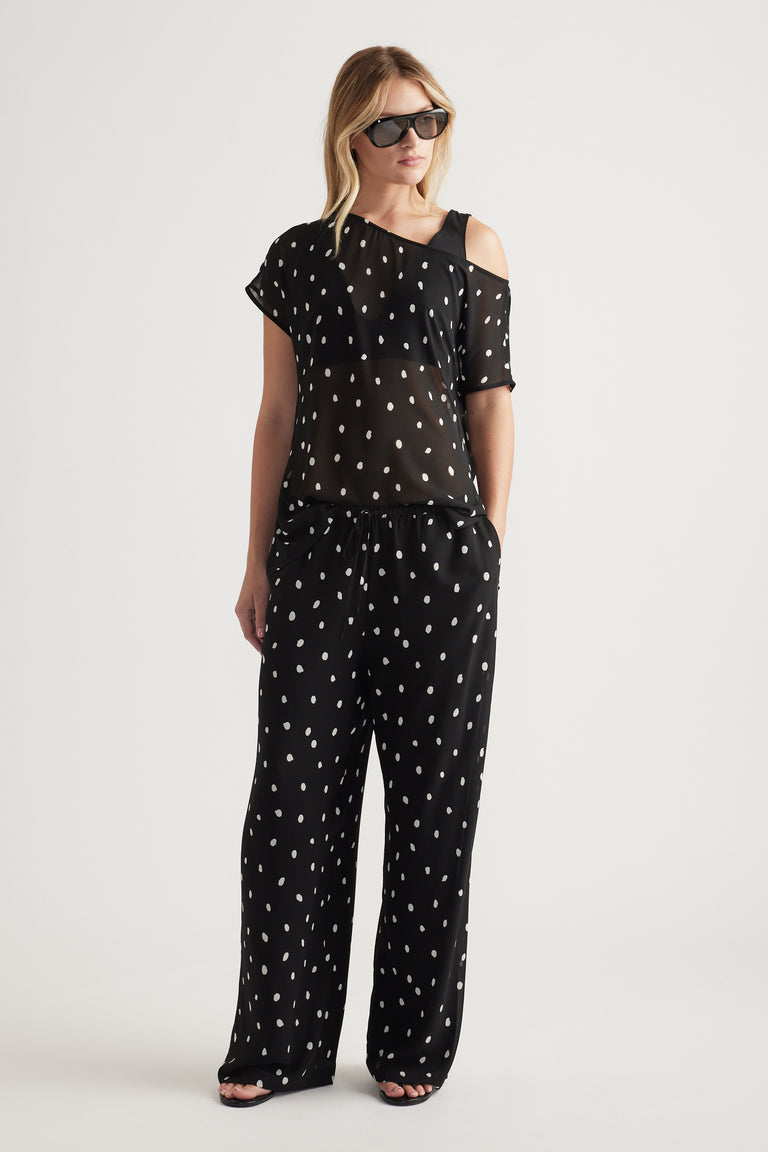Woman wearing black wide-leg sheer pants with white spots paired with a matching sheer top and black sunglasses