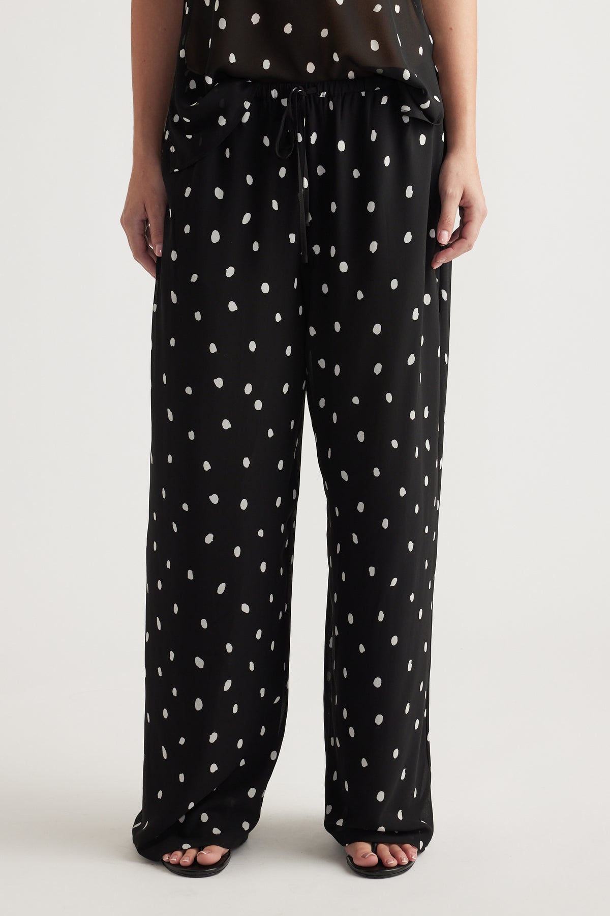 Woman wearing loose black pants with white spots and a drawstring waist paired with black open-toe sandals