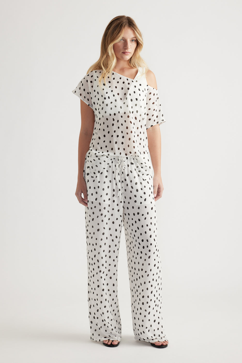 Woman wearing white sheer pants with black spots and a matching off-shoulder top for a relaxed, stylish look