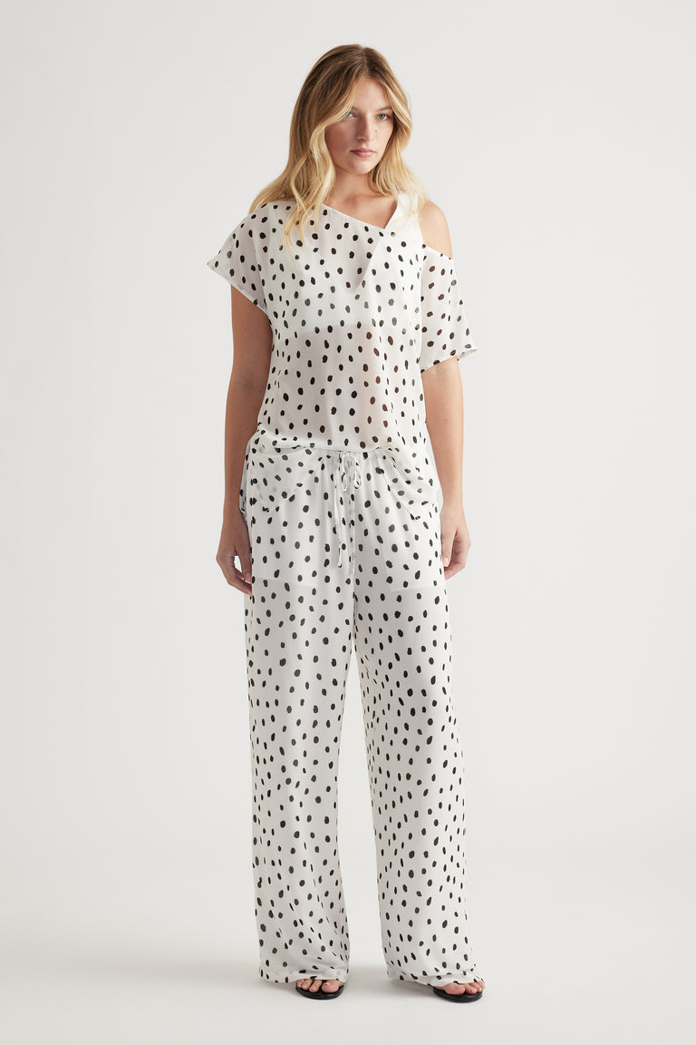 Woman wearing white sheer pants with black spots and a matching off-shoulder top for a relaxed, stylish look