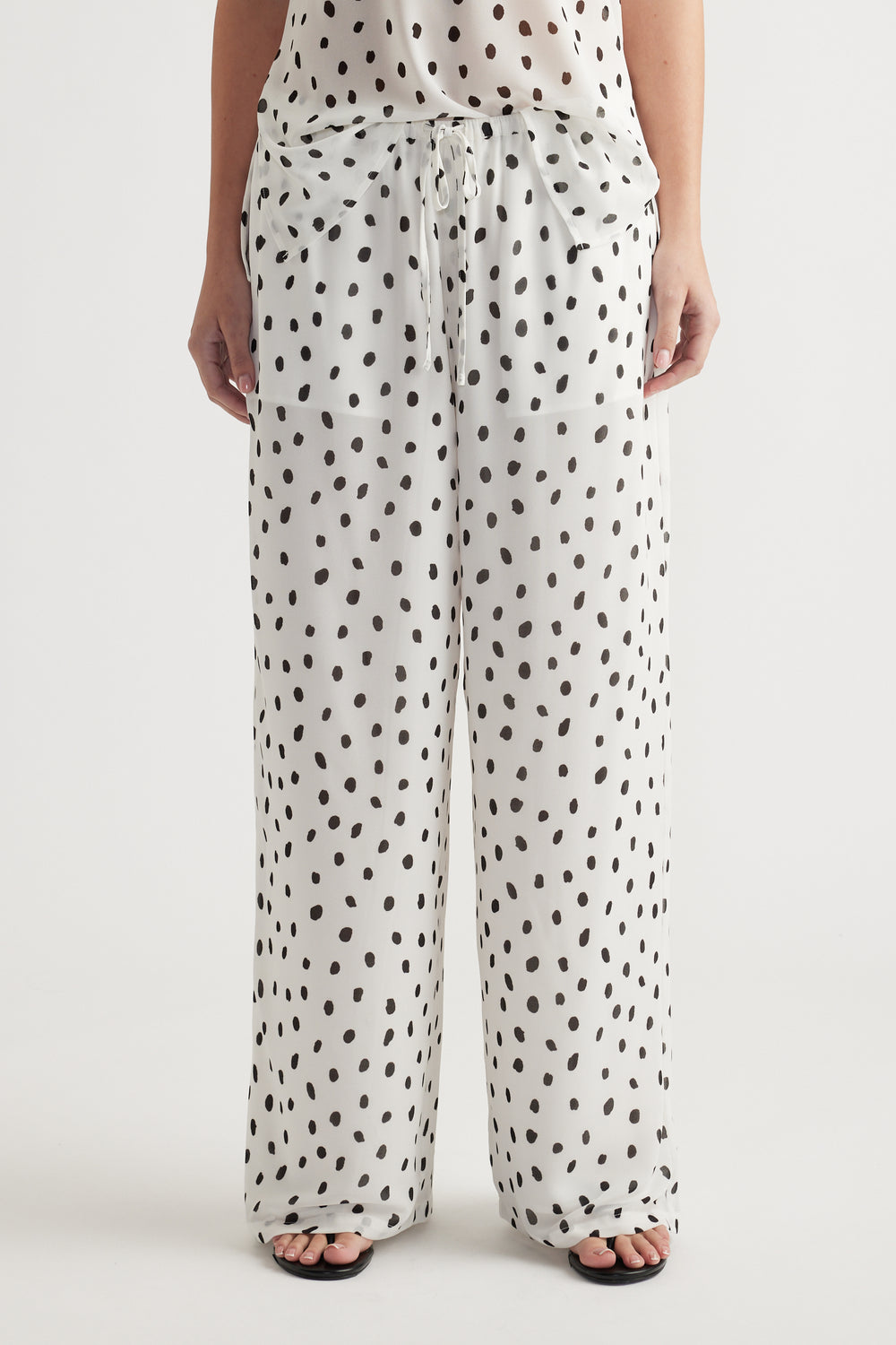 Woman wearing loose white pants with black irregular polka dots and a matching sheer top for a relaxed look