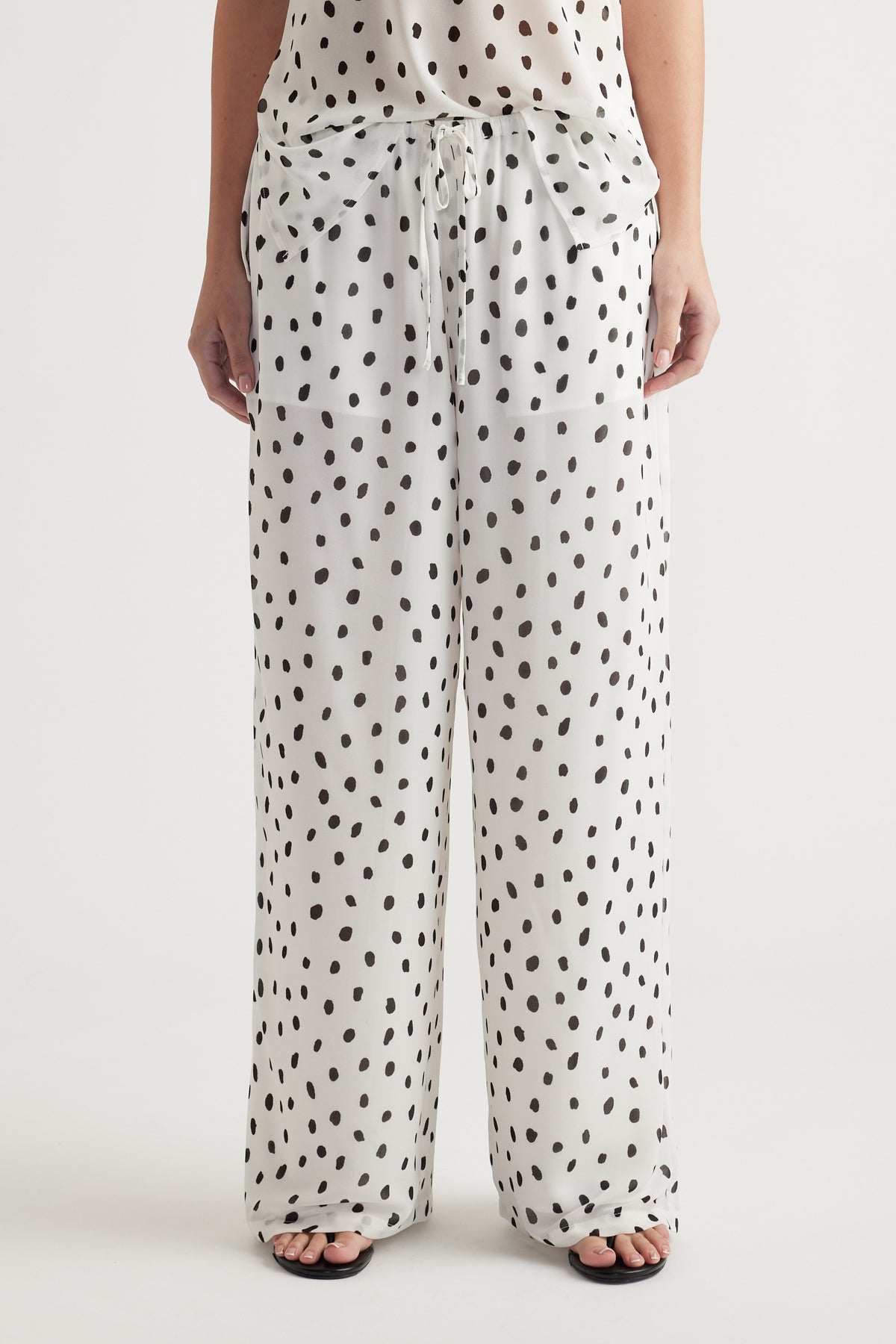 Woman wearing loose white pants with black irregular polka dots and a matching sheer top for a relaxed look