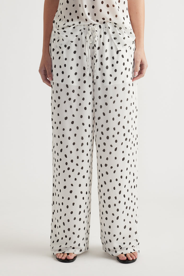 Woman wearing loose white pants with black irregular polka dots and a matching sheer top for a relaxed look