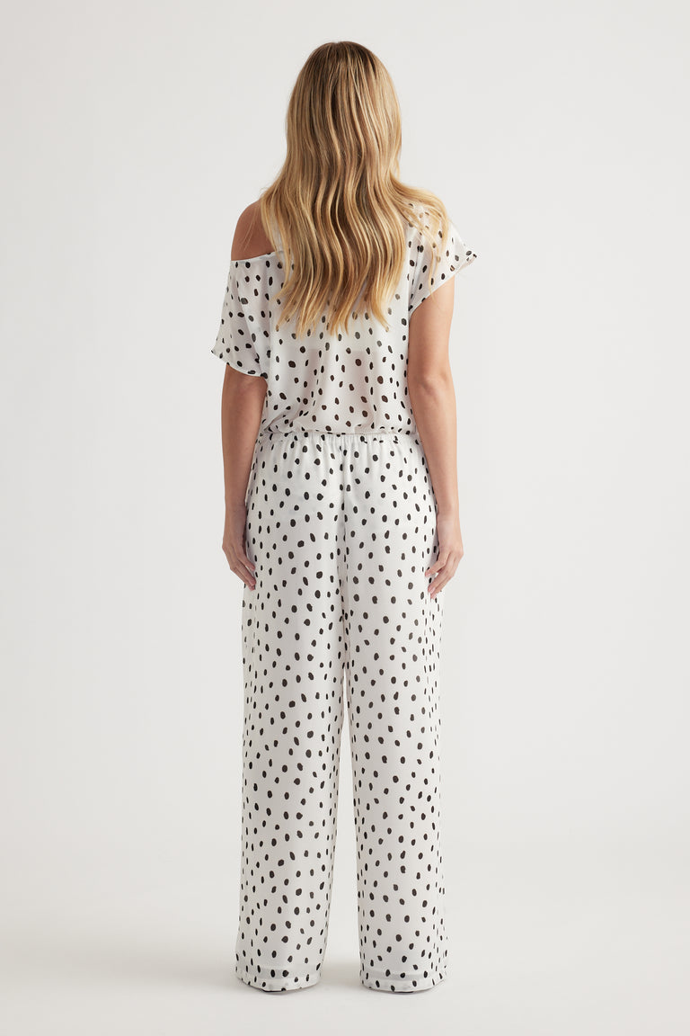 Woman wearing relaxed white wide-leg pants with a black spotted print paired with a loose off-shoulder top
