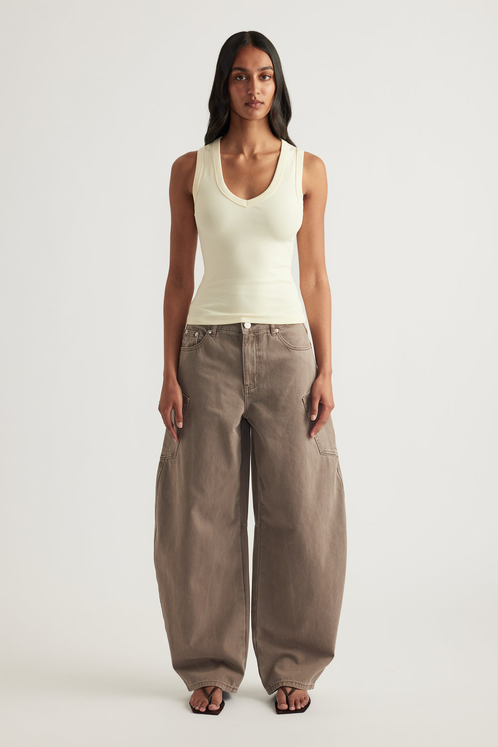Woman wearing a cream fitted sleeveless tank with a low V neckline and wide leg taupe pants