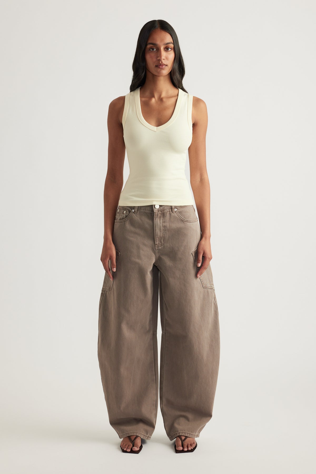 Woman wearing a cream fitted sleeveless tank with a low V neckline and wide leg taupe pants