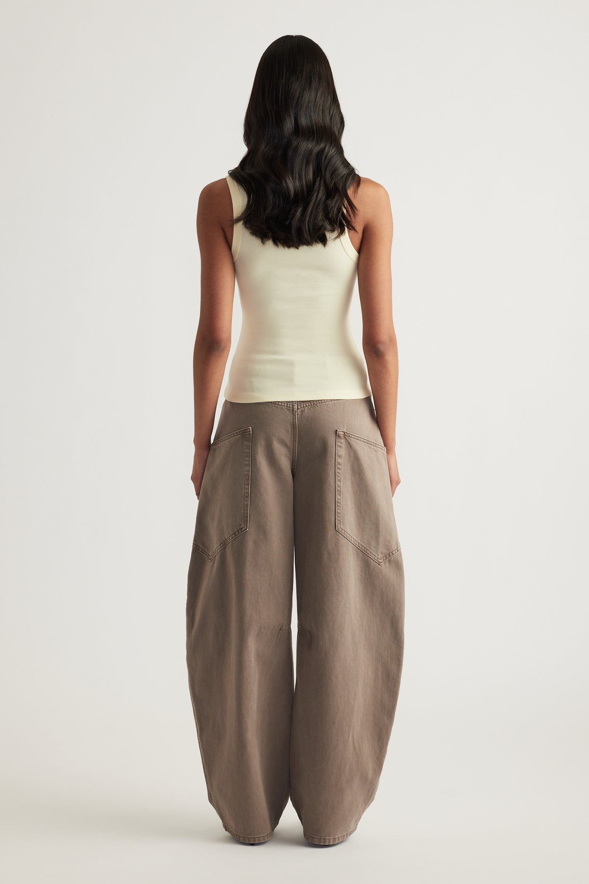 Woman viewed from behind wearing a cream fitted sleeveless tank with taupe wide leg pants