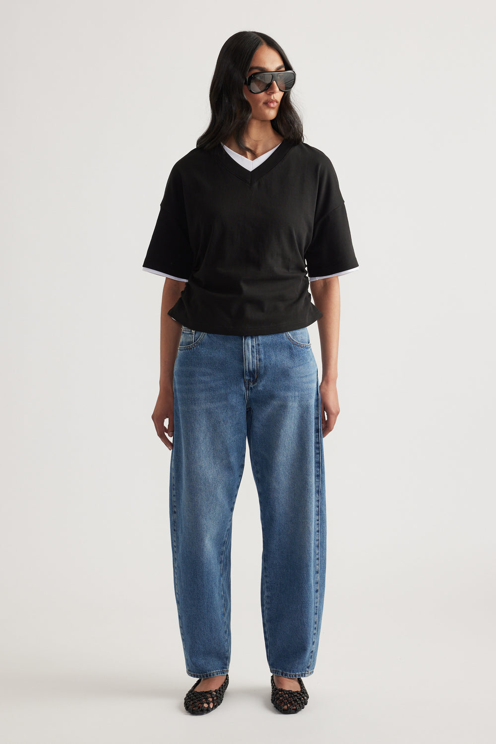 Woman in a black relaxed V-neck short sleeve tee, blue jeans and sunglasses