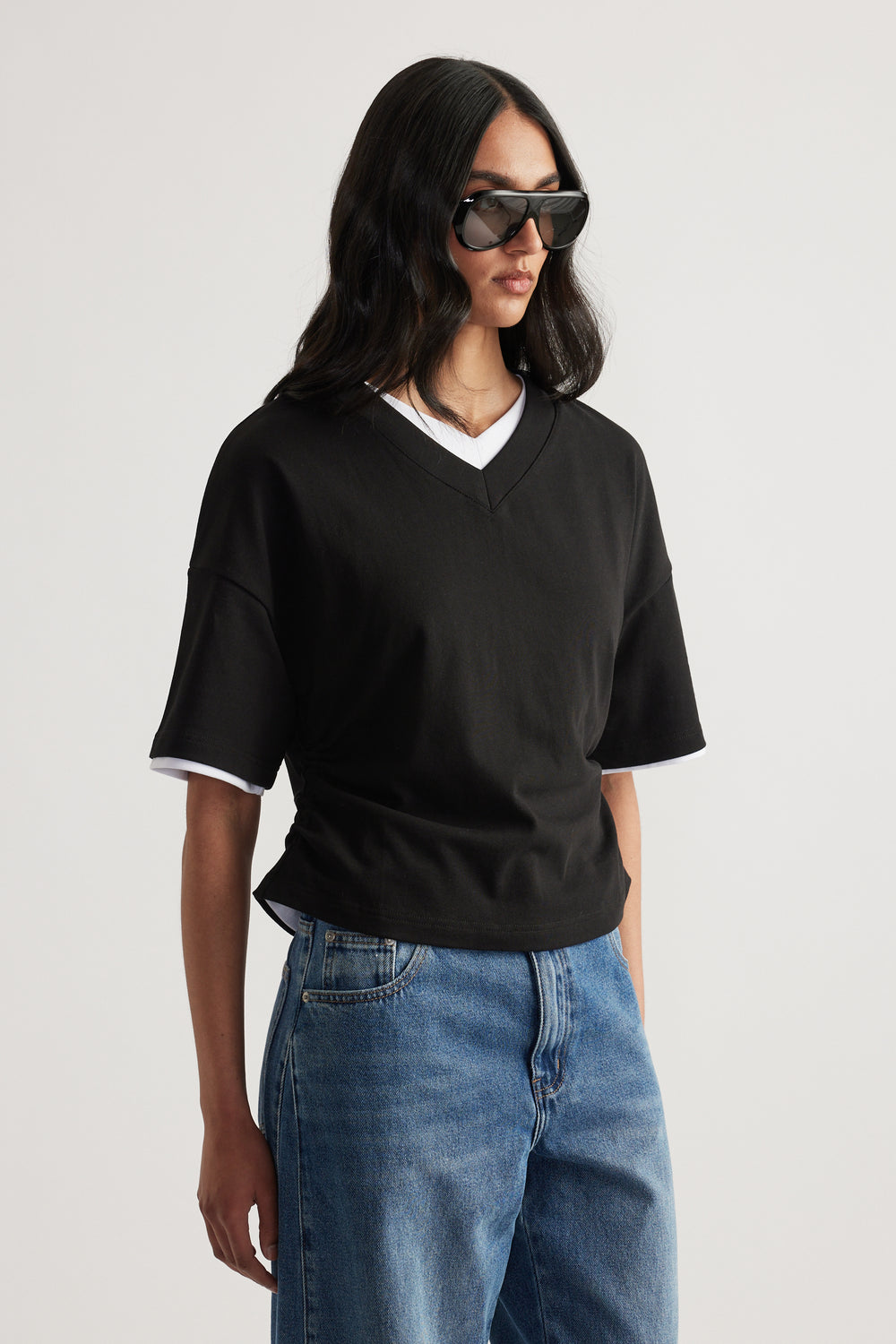 Woman wearing a black V-neck tee with white trim, relaxed jeans and sunglasses