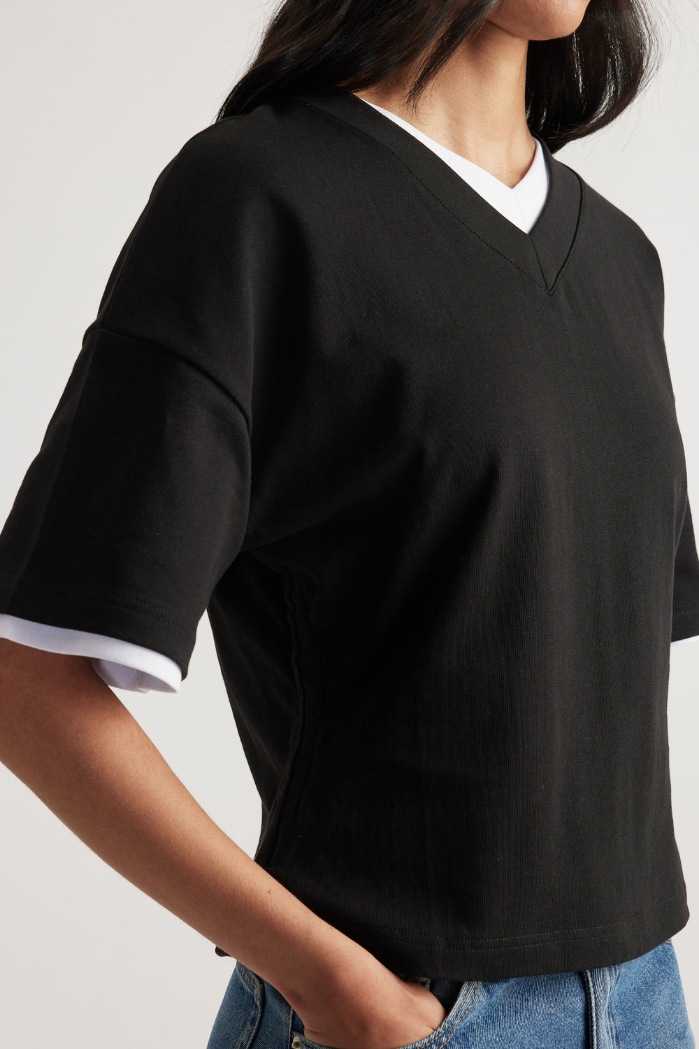 Woman wearing a relaxed black V-neck boxy tee layered over a white top with blue jeans