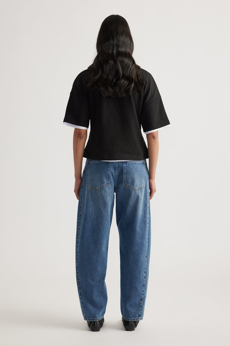 Woman viewed from behind wearing a black boxy short sleeve tee and relaxed blue jeans