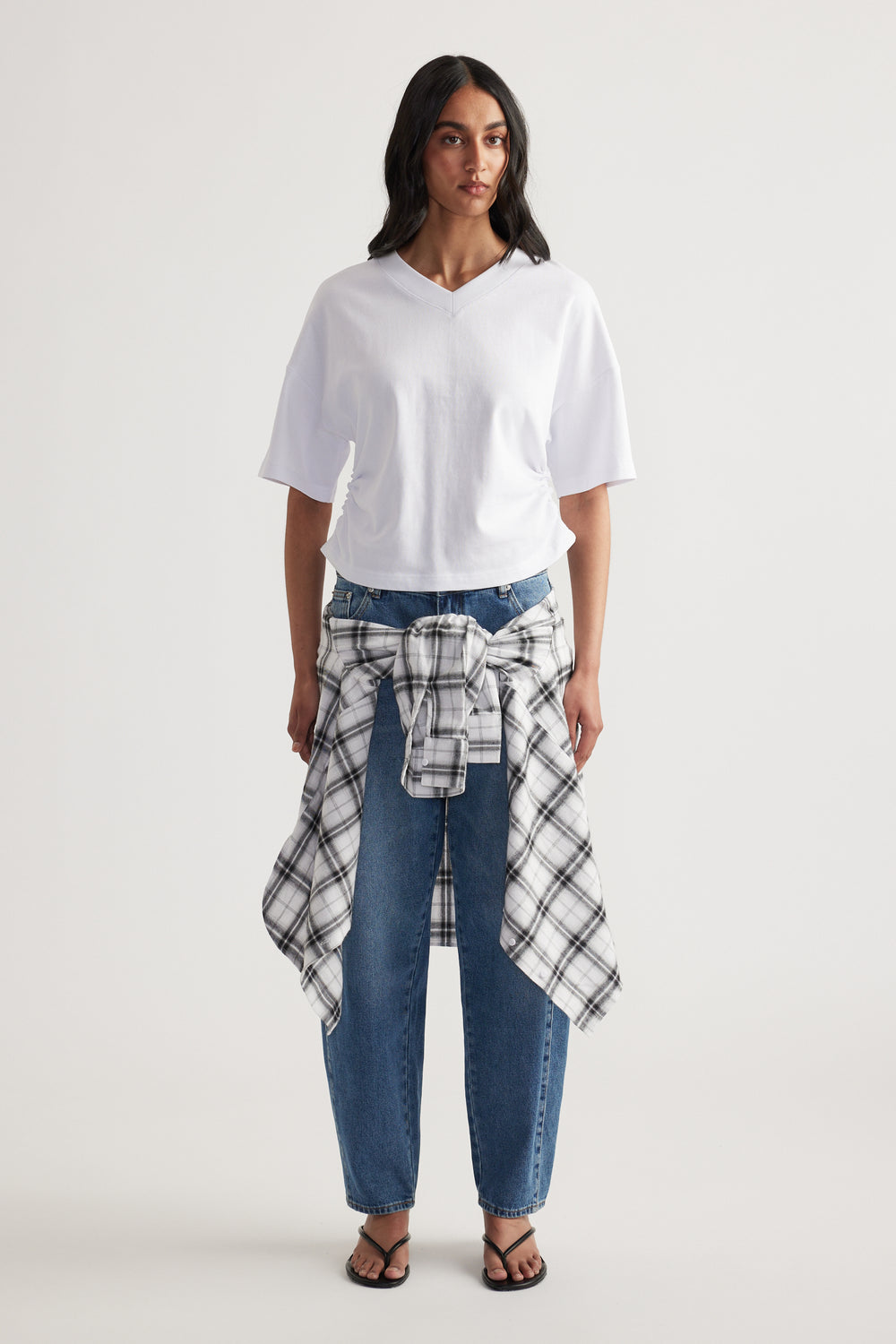 Woman wearing a white boxy V-neck tee with blue jeans and a plaid shirt tied at the waist