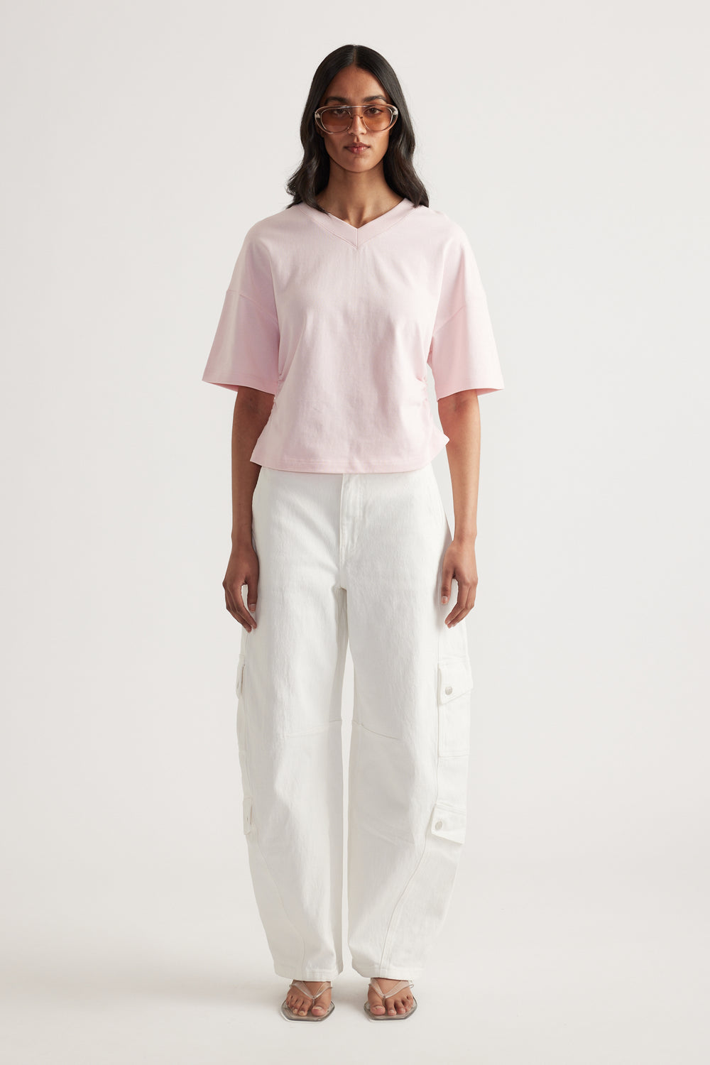 Woman wearing a relaxed pink V-neck tee with white cargo pants and strappy sandals