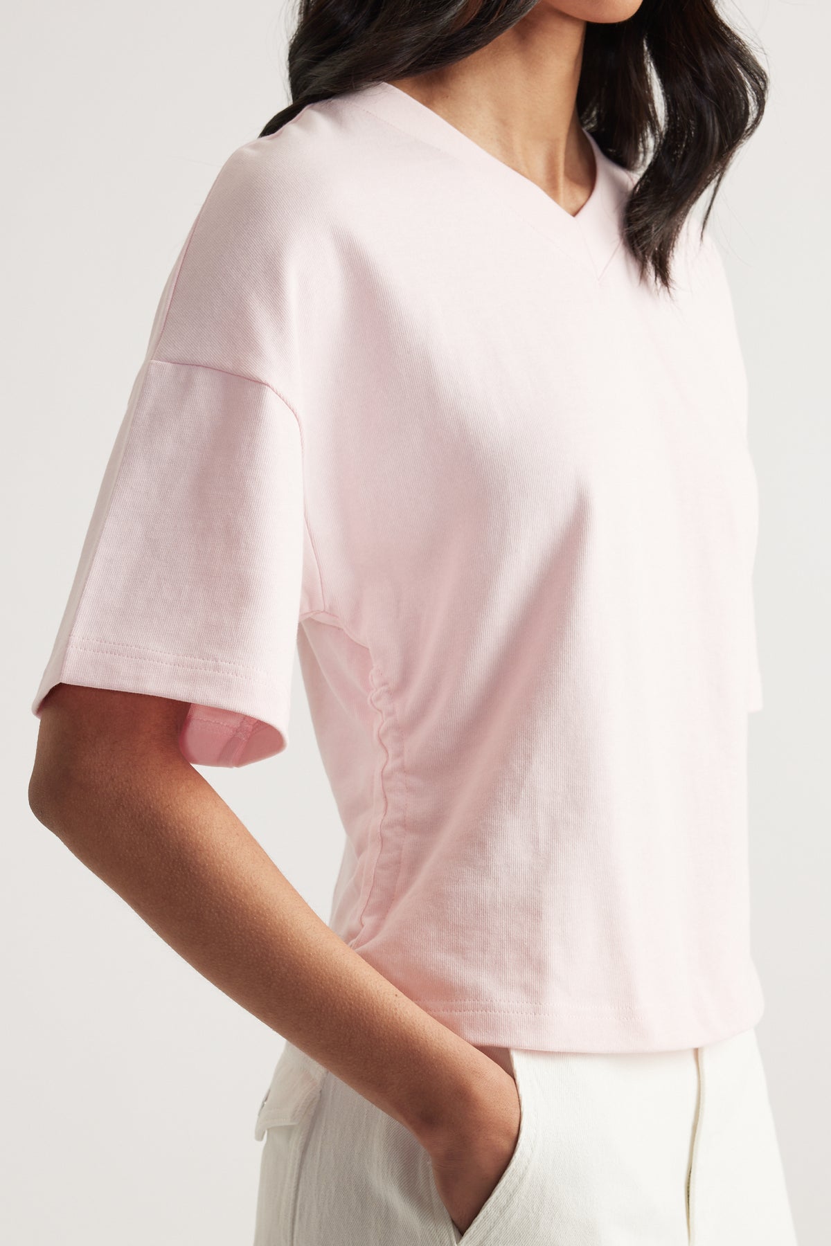 Woman wearing a pale pink boxy V-neck tee with white pants