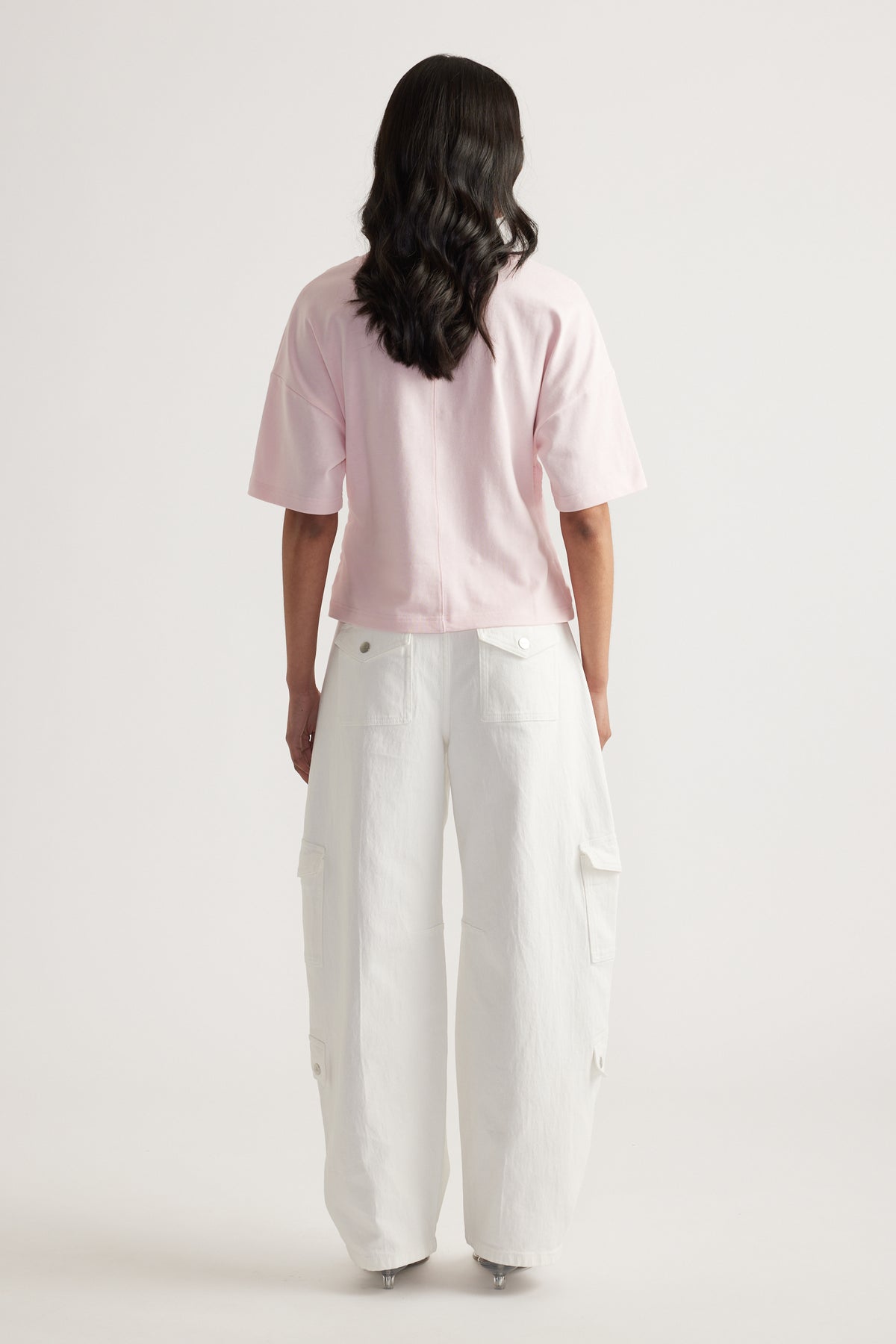 Back view of a woman wearing a relaxed pink boxy tee with white cargo pants