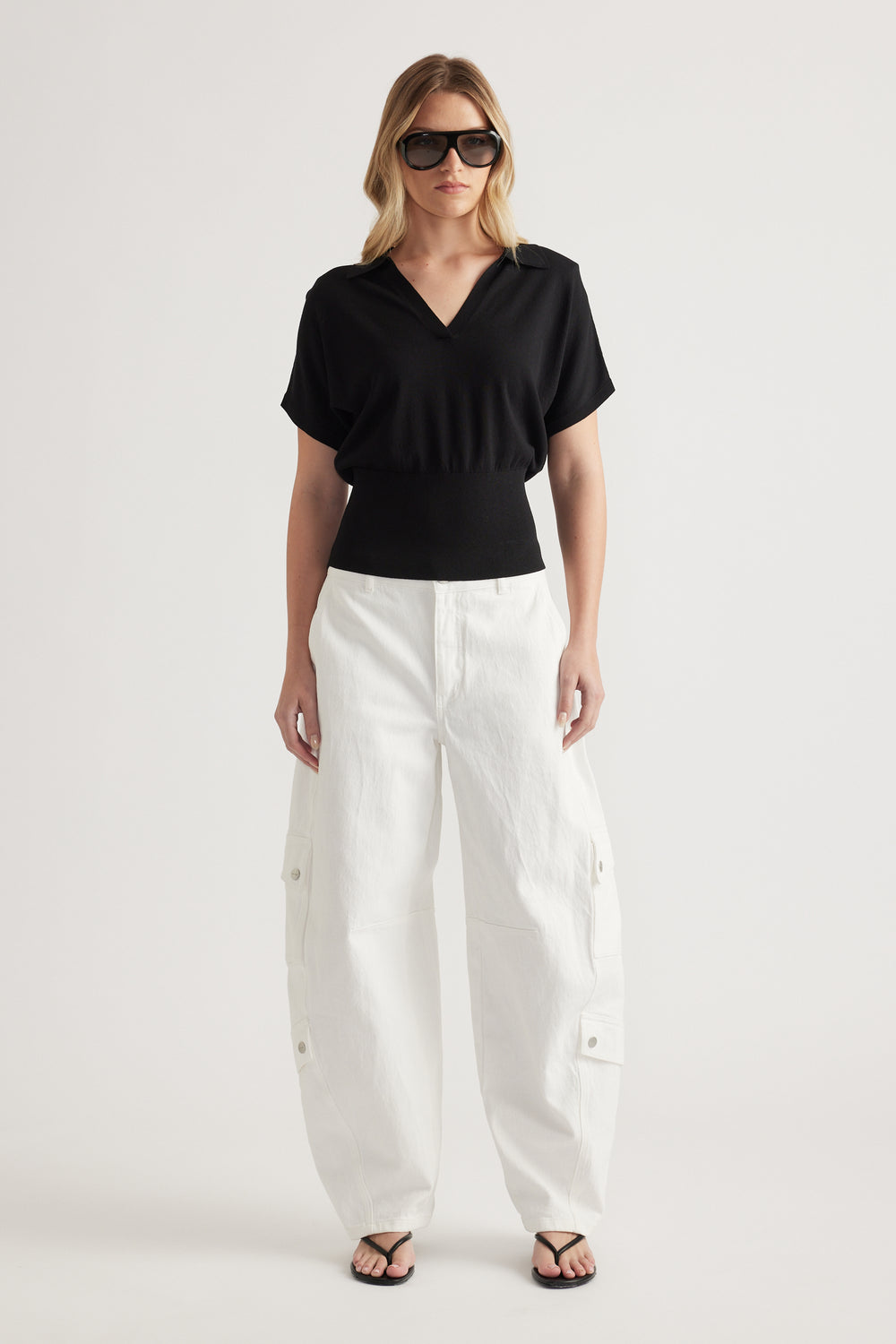 Woman wearing a black short sleeve V neck knit top with white cargo pants and sandals