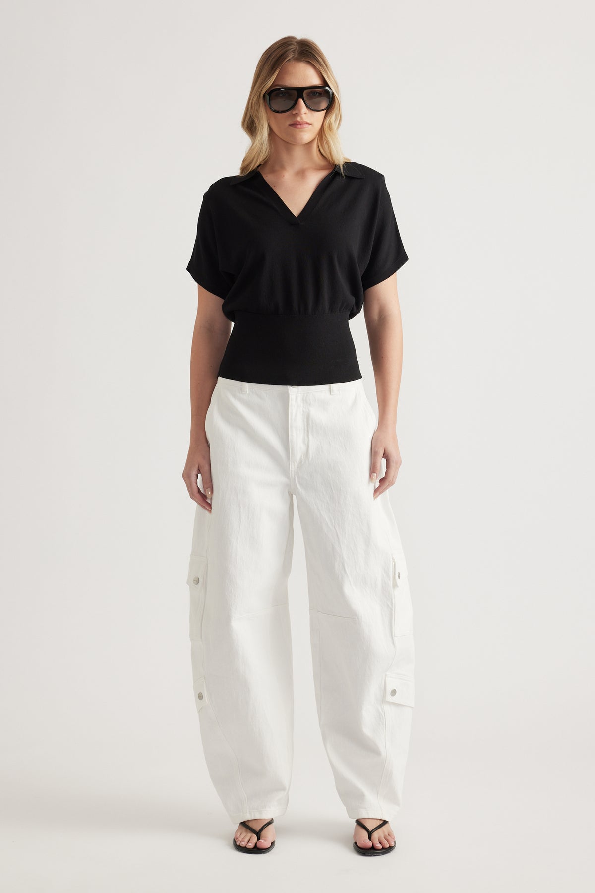 Woman wearing a black short sleeve V neck knit top with white cargo pants and sandals