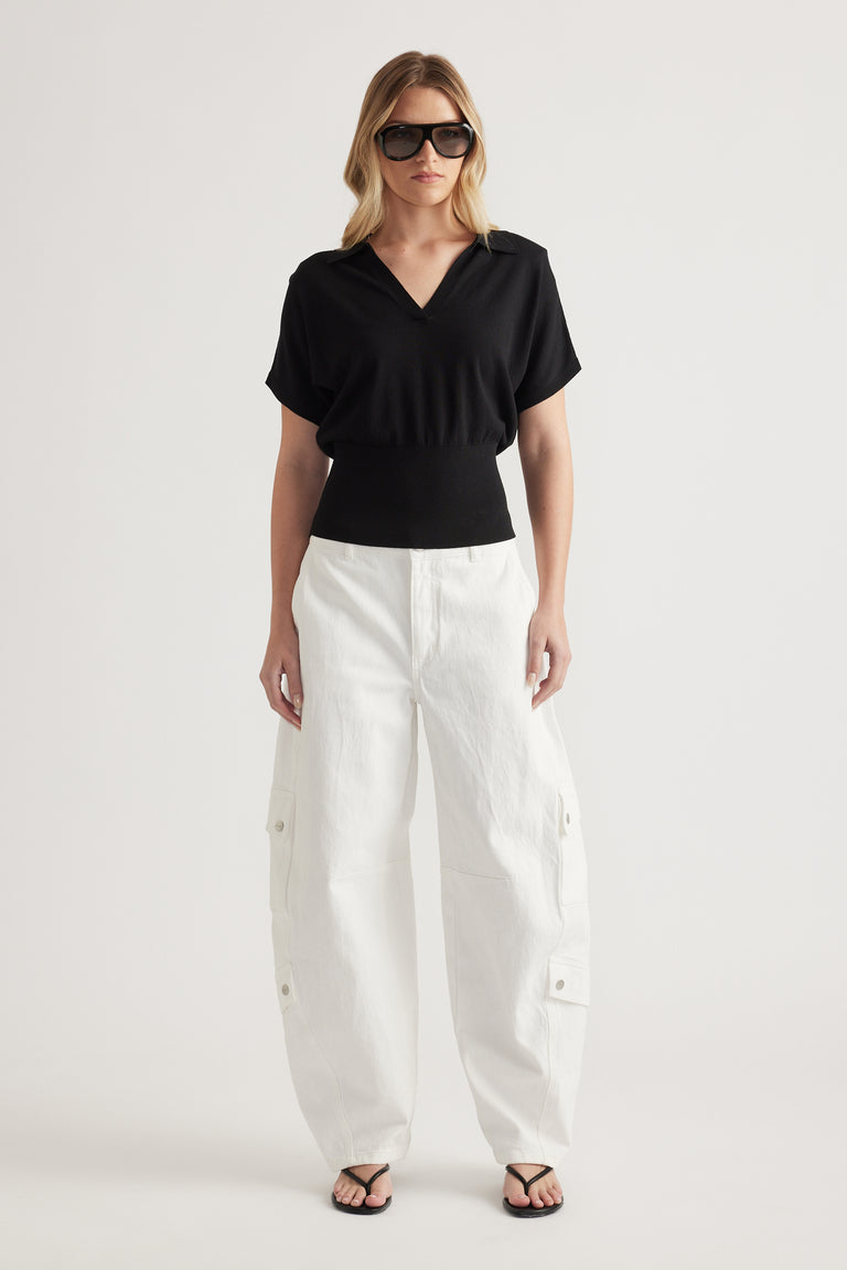 Woman wearing a black short sleeve V neck knit top with white cargo pants and sandals