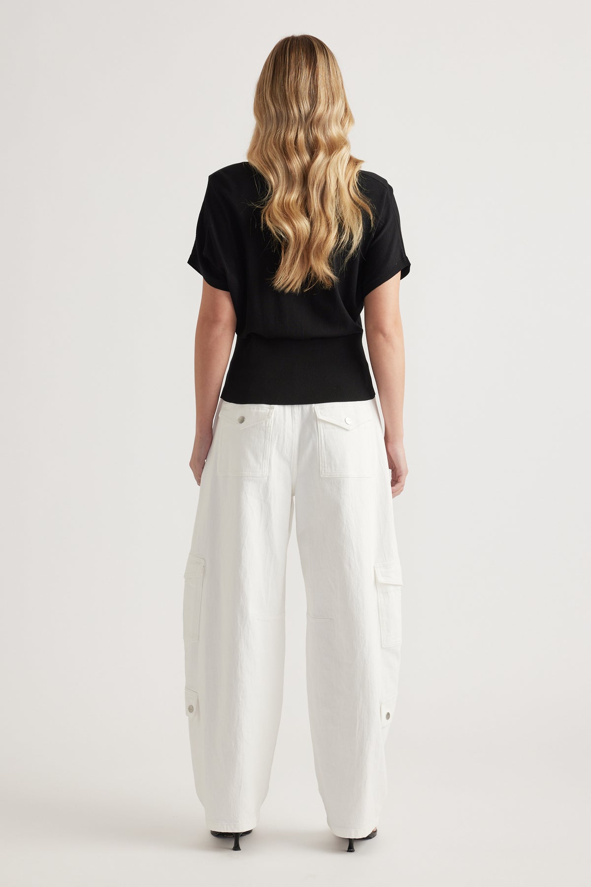 Woman wearing a black short sleeve polo knit top with white cargo pants