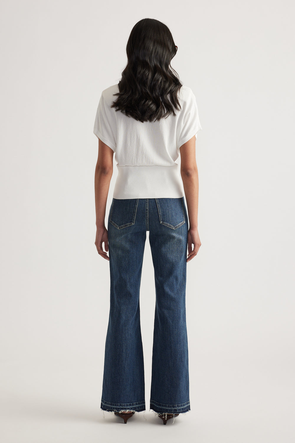 Back view of a woman wearing a white short sleeve collared knit top with a cinched waist and wide leg jeans