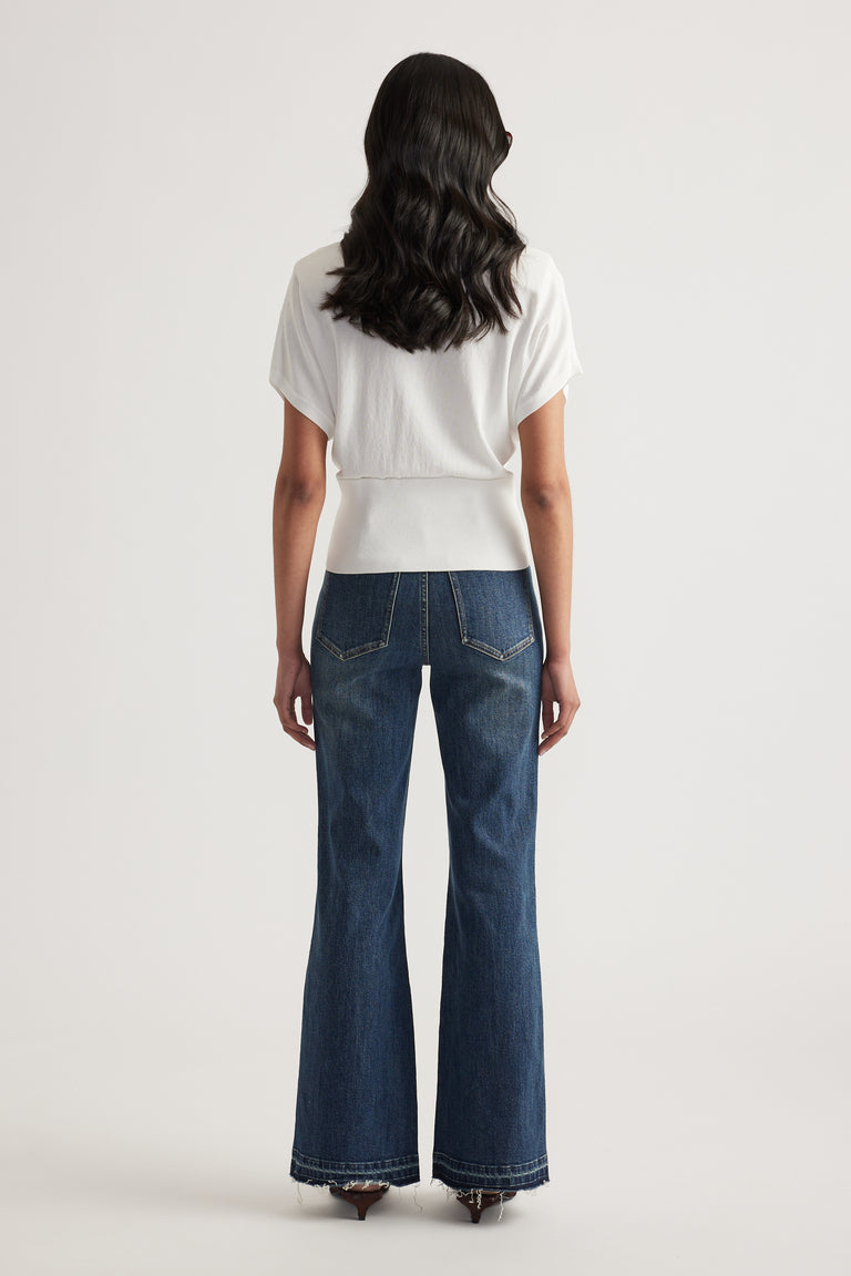 Back view of a woman wearing a white short sleeve collared knit top with a cinched waist and wide leg jeans