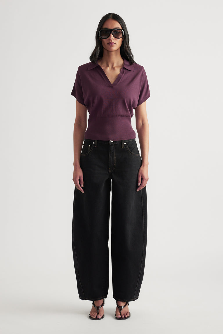 Woman wearing a burgundy short sleeve collared V neck knit top with black wide leg jeans and sunglasses