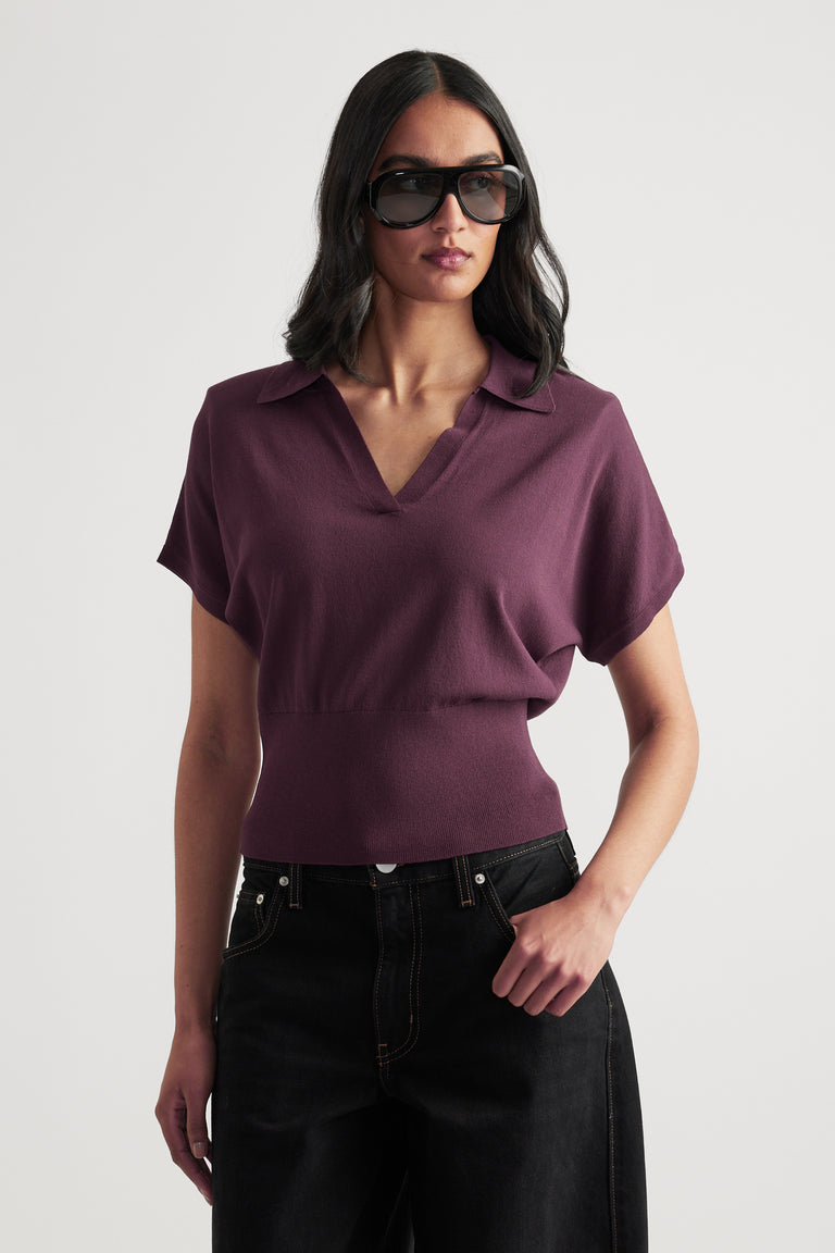 Woman in a plum short sleeve collared V-neck knit top with a cinched waist, black jeans and sunglasses