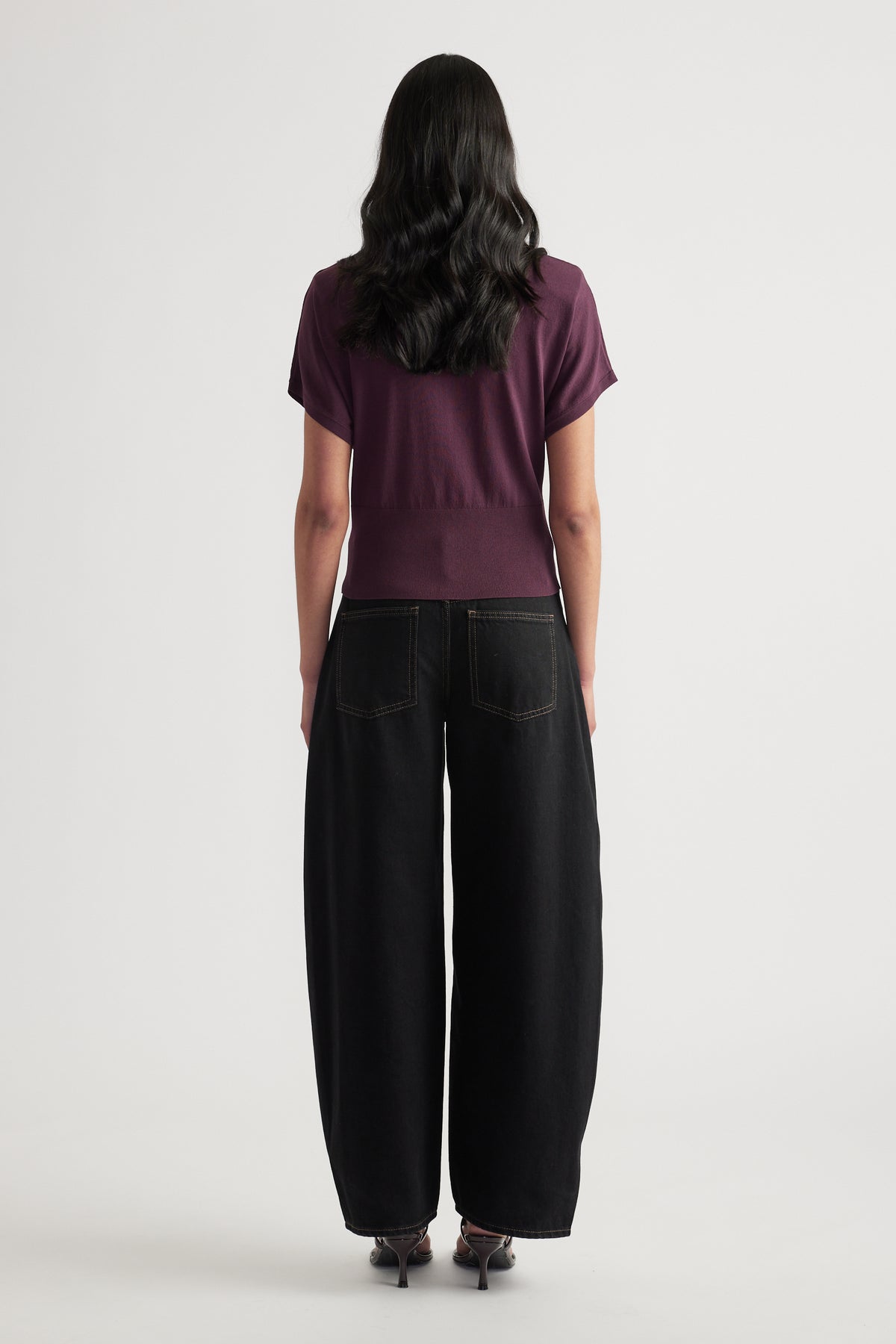Back view of a woman wearing a plum short sleeve knit polo top with black wide leg pants