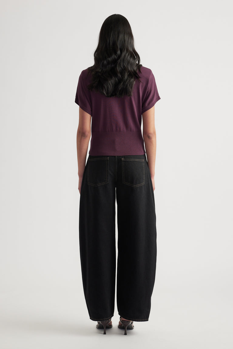 Back view of a woman wearing a plum short sleeve knit polo top with black wide leg pants