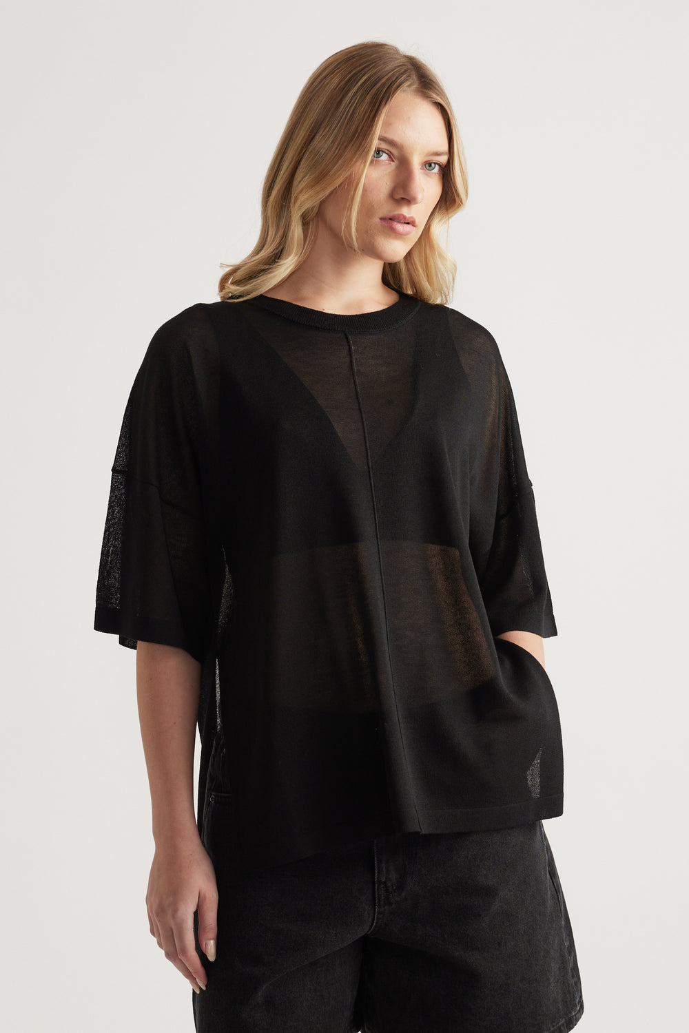 Woman wearing a relaxed black sheer knit tee with short sleeves and crew neck, styled with black jeans