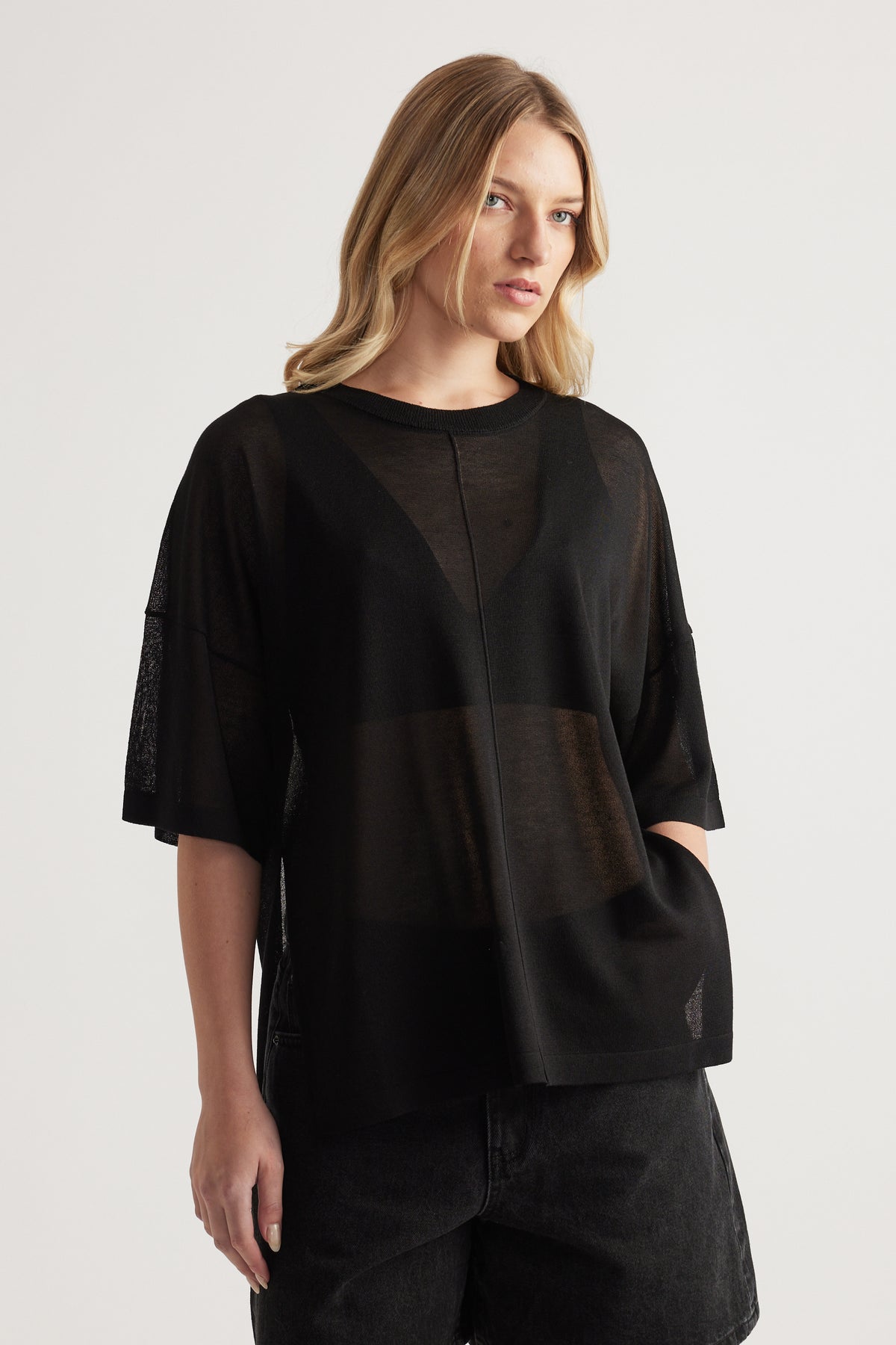 Woman wearing a relaxed black sheer knit tee with short sleeves and crew neck, styled with black jeans