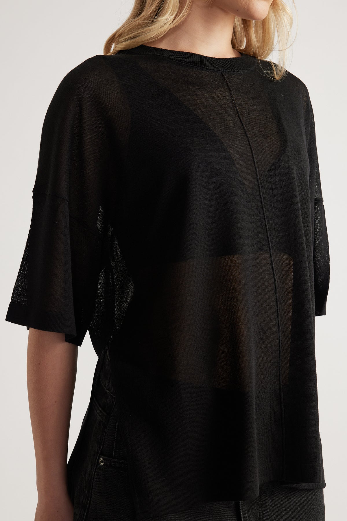 Woman wearing a black sheer oversized knit tee with short sleeves, crew neck and center seam detail