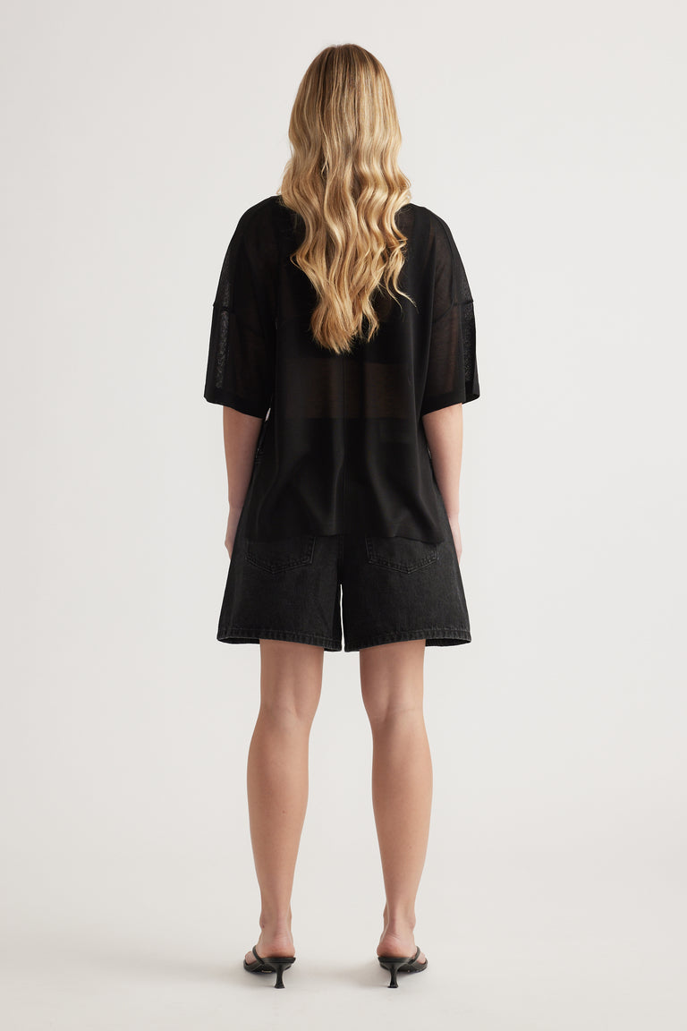 Back view of woman wearing a relaxed black longline knit tee with short sleeves and sheer detailing