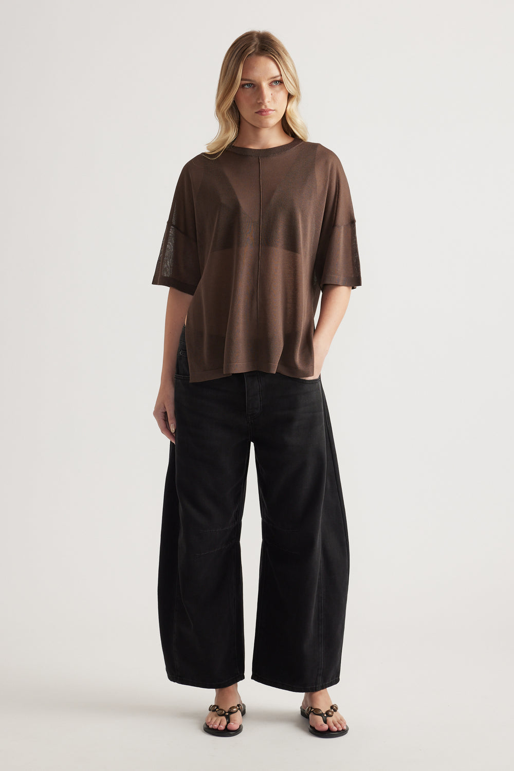 Woman wearing a relaxed brown sheer knit tee with black wide leg pants and strappy sandals