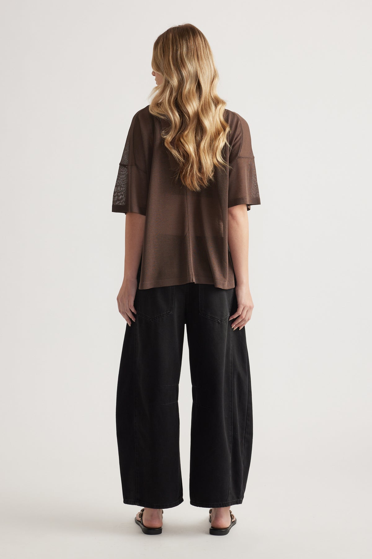 Back view of woman wearing a relaxed brown oversized knit tee with short sleeves and black wide leg pants