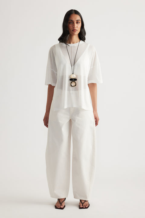 Woman wearing a sheer white oversized knit tee with wide leg white pants and layered pendant necklace