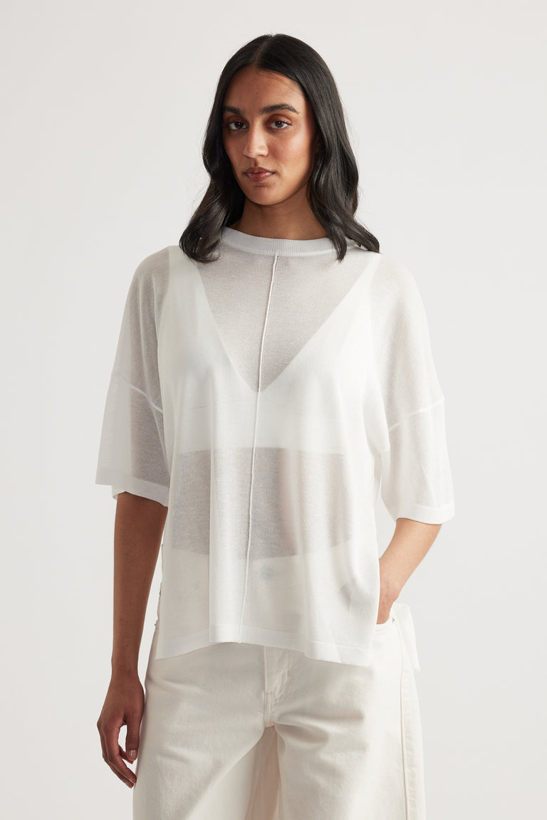 Woman wearing a sheer white oversized knit tee with short sleeves and white pants over a tank top