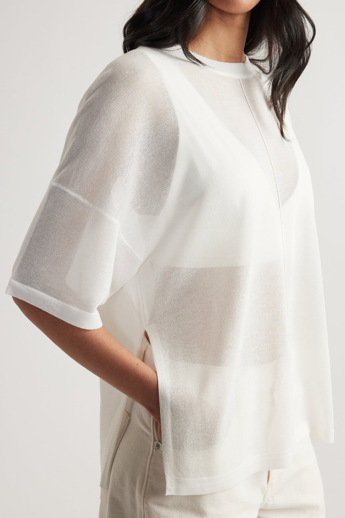 Woman wearing an ivory sheer oversized knit tee with crew neck, short sleeves and relaxed longline fit