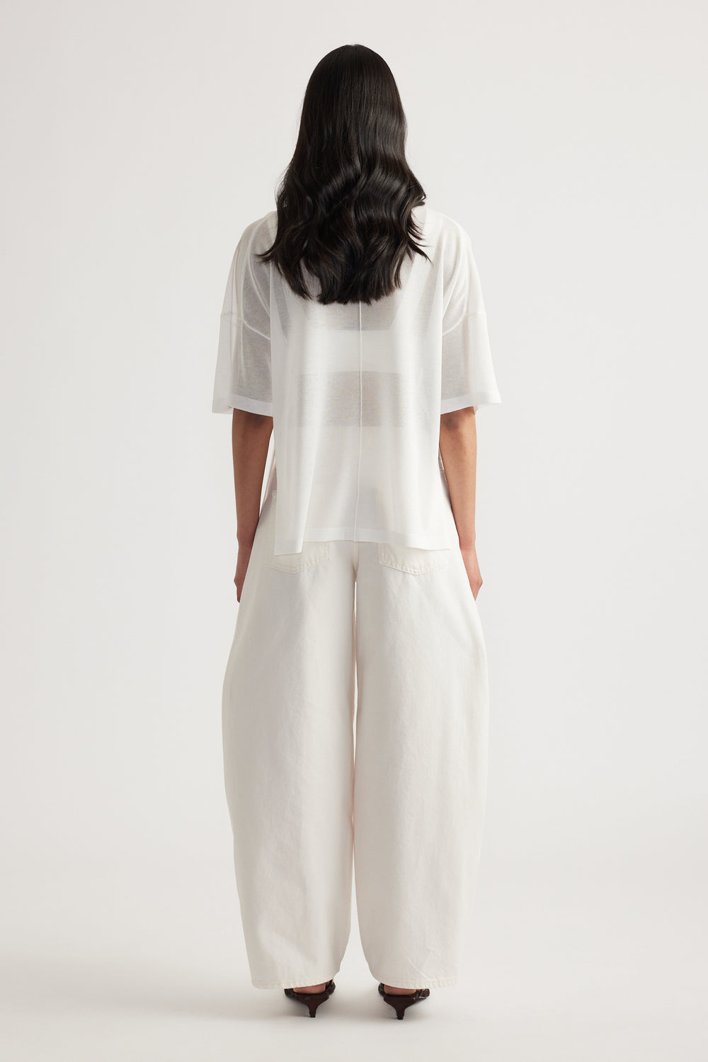 Back view of woman wearing a sheer white relaxed fit longline knit tee with short sleeves and wide leg pants