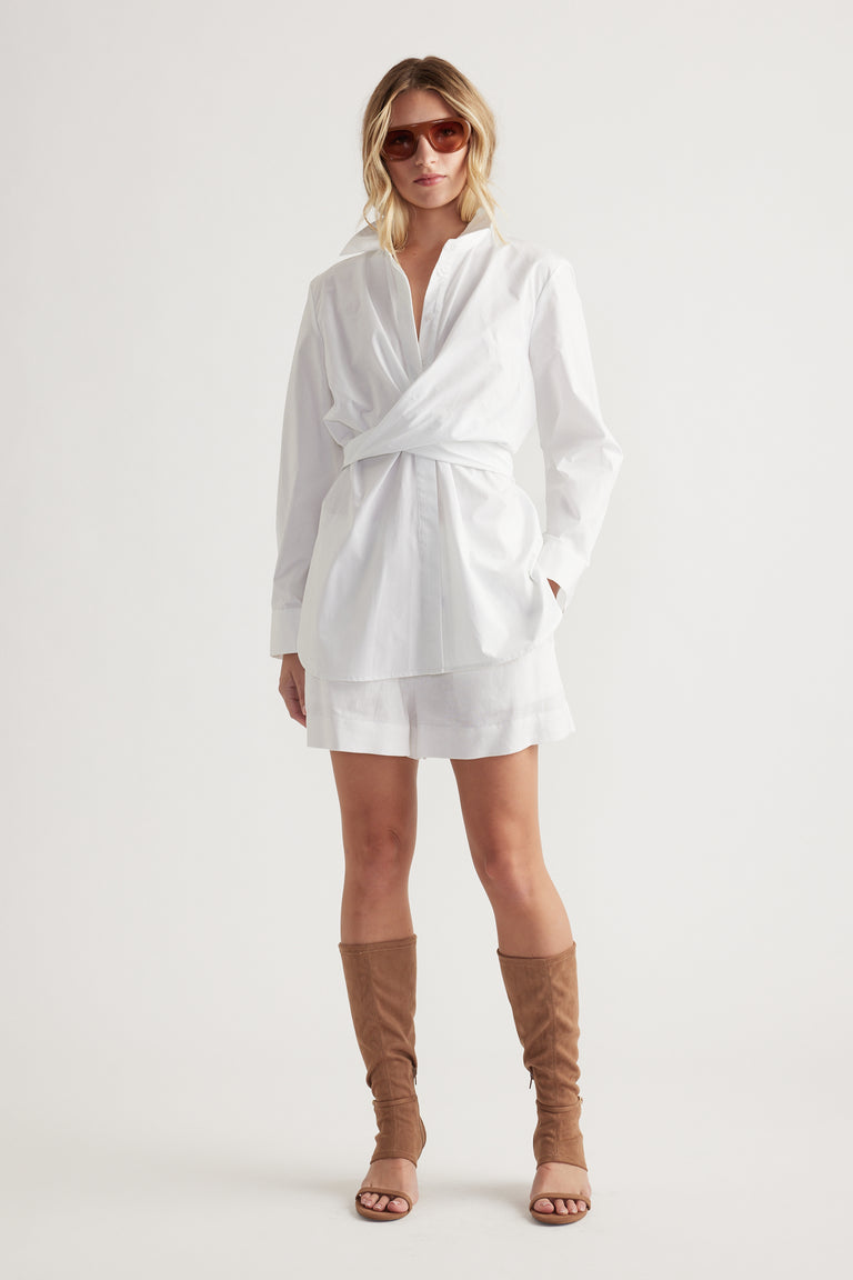 Woman wearing white linen blend shorts paired with a loose white wrap shirt and tan knee-high open-toe boots.