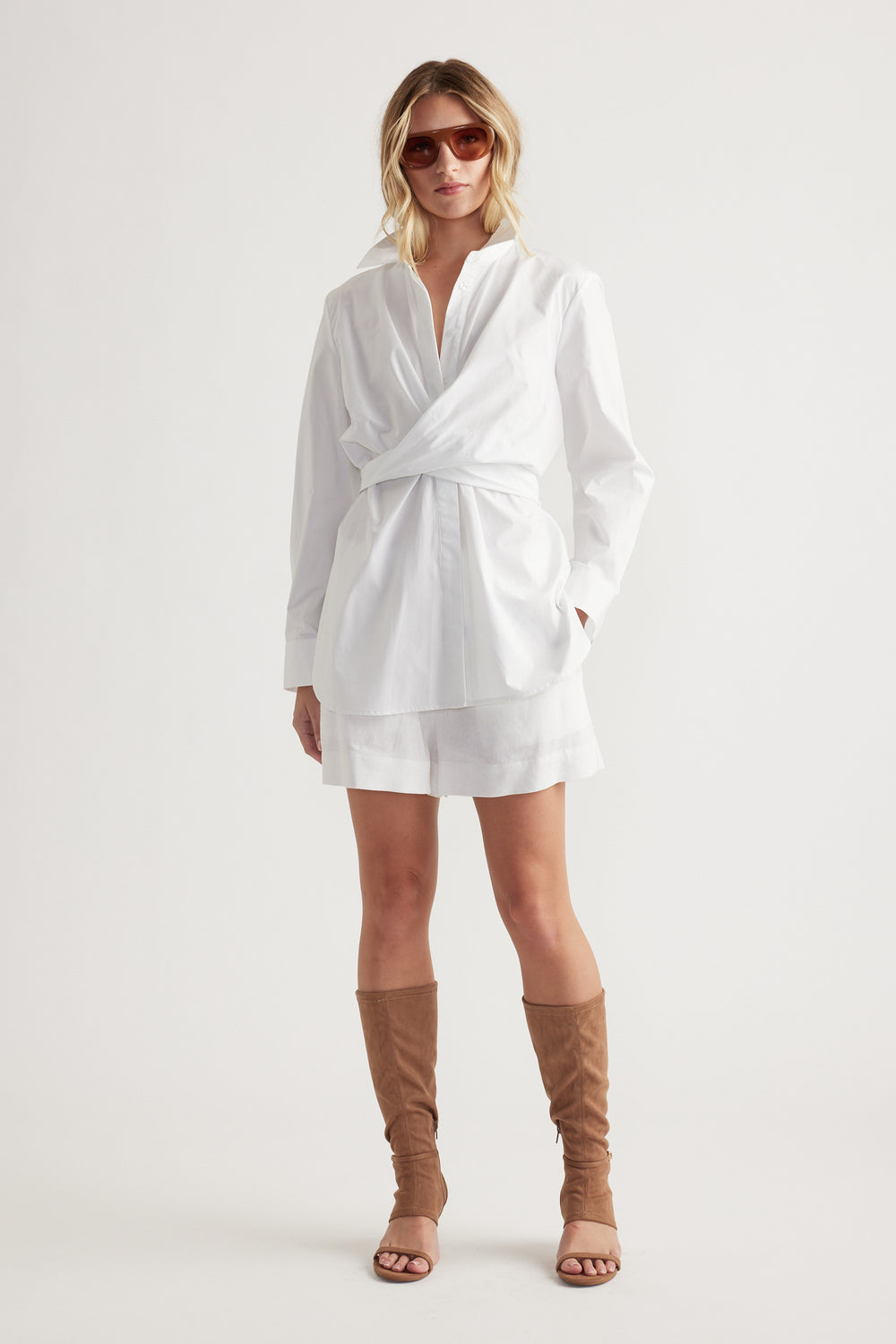 Woman wearing a white wrap-style shirt dress paired with tan suede buckle detail heels and oversized sunglasses