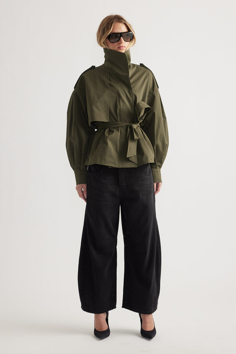 Woman wearing high-waisted wide-leg black jeans paired with an olive belted jacket and oversized sunglasses