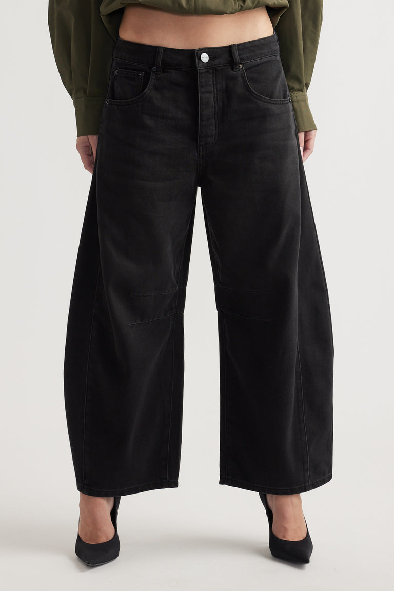 High-rise wide-leg black denim jeans with subtle panel detailing, styled with black pointed heels and a cropped top.