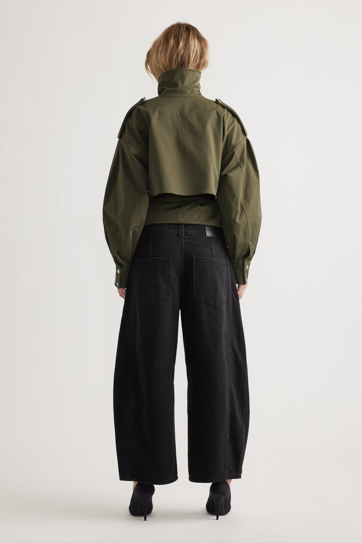 Back view of woman wearing loose black wide-leg jeans paired with structured olive green cropped jacket