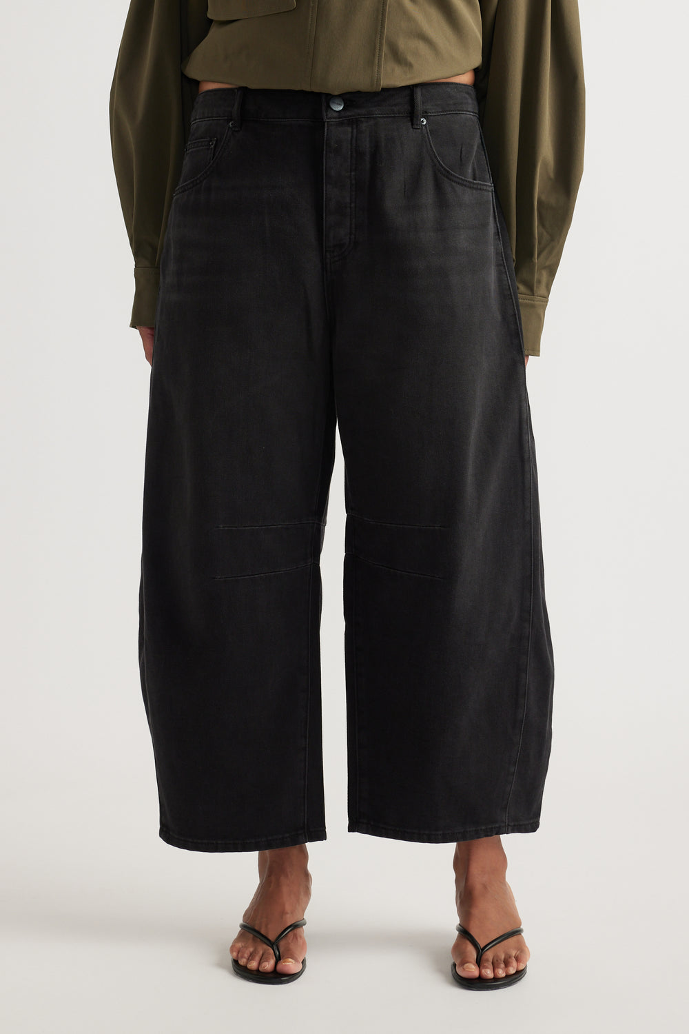 Woman wearing high rise black cropped barrel jeans with an olive shirt and strappy flat sandals