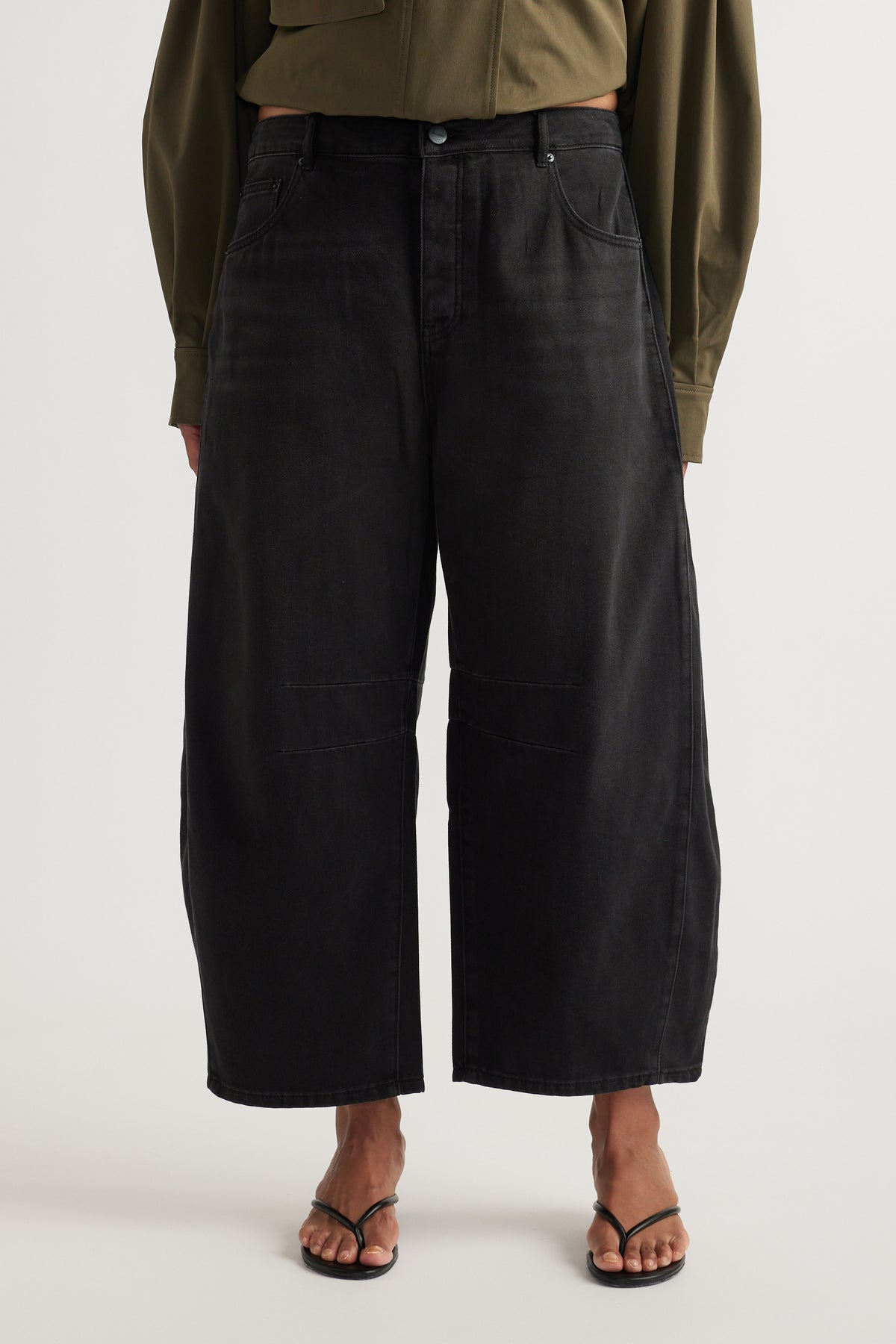 Woman wearing high rise black cropped barrel jeans with an olive shirt and strappy flat sandals