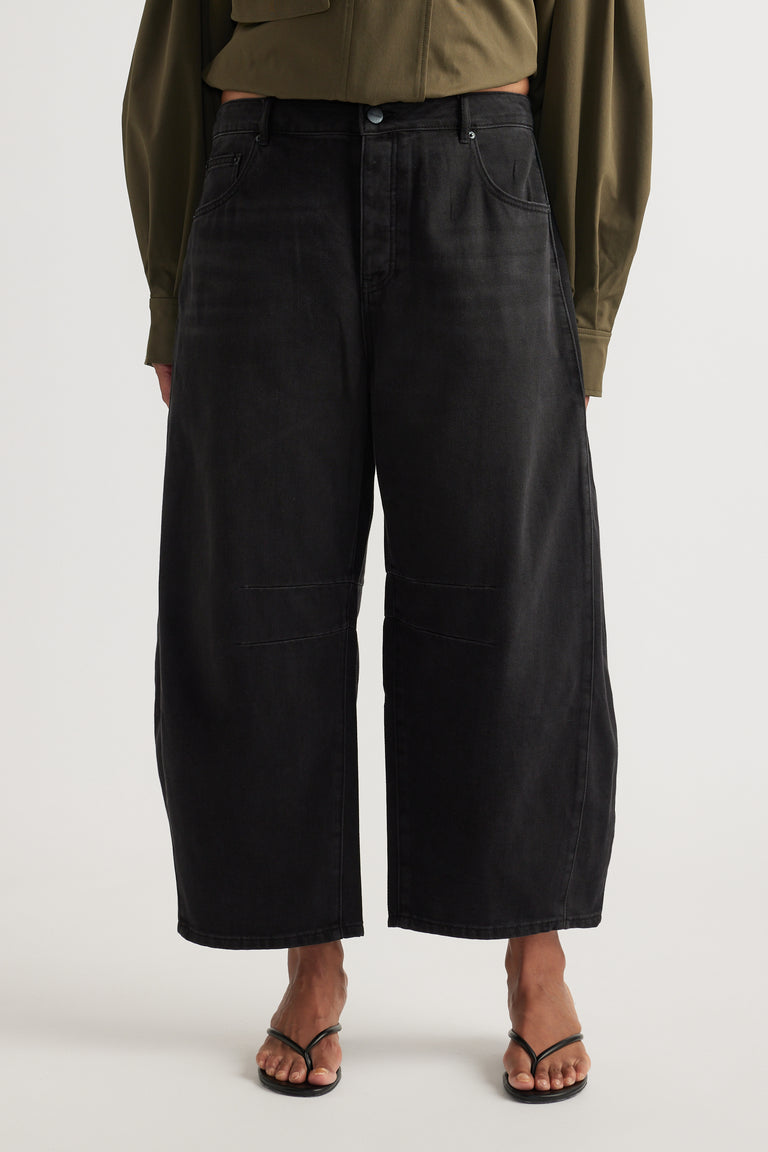 Woman wearing high rise black cropped barrel jeans with an olive shirt and strappy flat sandals