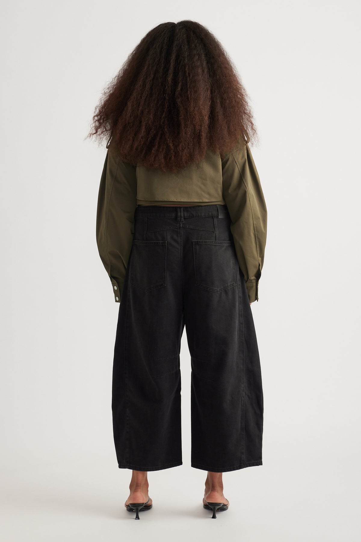 Back view of woman in black cropped barrel jeans, olive jacket and kitten heels