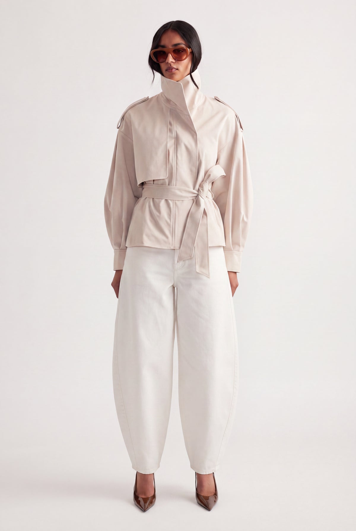 Woman wearing white mid rise barrel jeans with a belted cream jacket and pointed heels