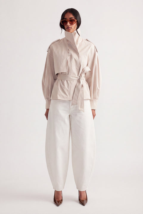Woman wearing white mid rise barrel jeans with a belted cream jacket and pointed heels